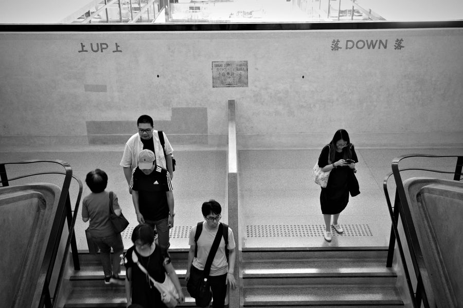People riding up and down escalators, in black and white