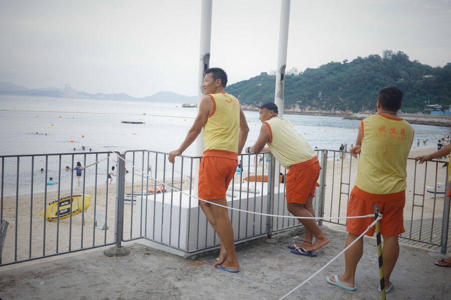 Lifeguards in yellow and orange leaning on a railing by the beach