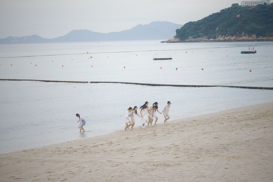 Kids running along the shoreline of a beach below green hills